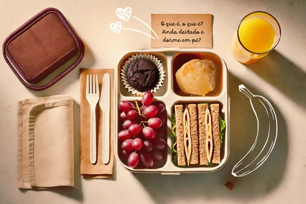 lancheira escolar sobre uma mesa com talheres e um copo de suco - charadas infantis engraçadas