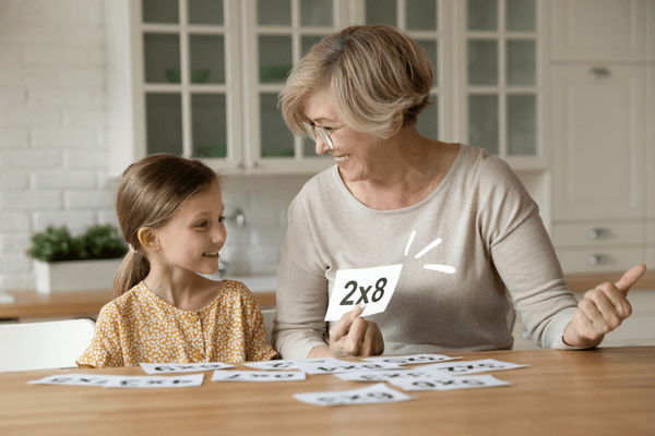Avó ensinando tabuada a neta usando cartões de multiplicação – ordem correta para ensinar multiplicação.